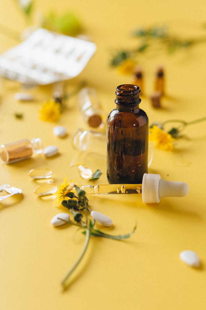 services-02 Brown glass dropper bottle among herbs and pills on yellow surface, ideal for wellness themes.